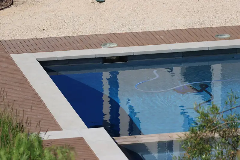 Pool vacuum hose in the water beside a wood deck